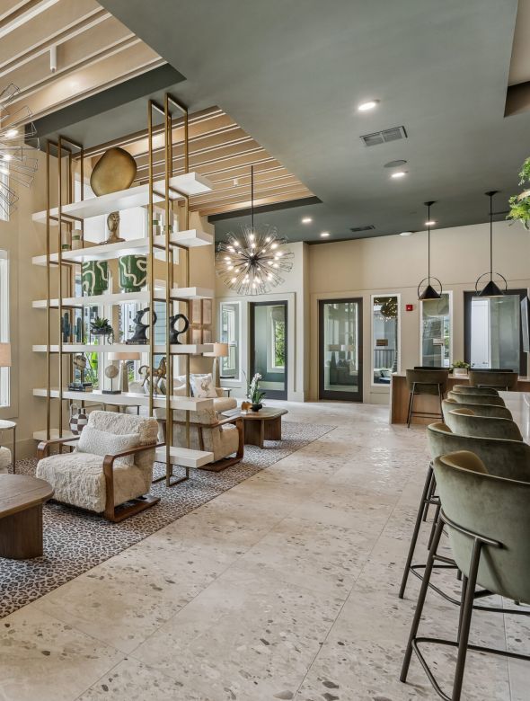 Modern lounge with cozy seating, stylish lighting, open shelving, large windows, and a bar area on the right. Neutral colors and elegant decor.