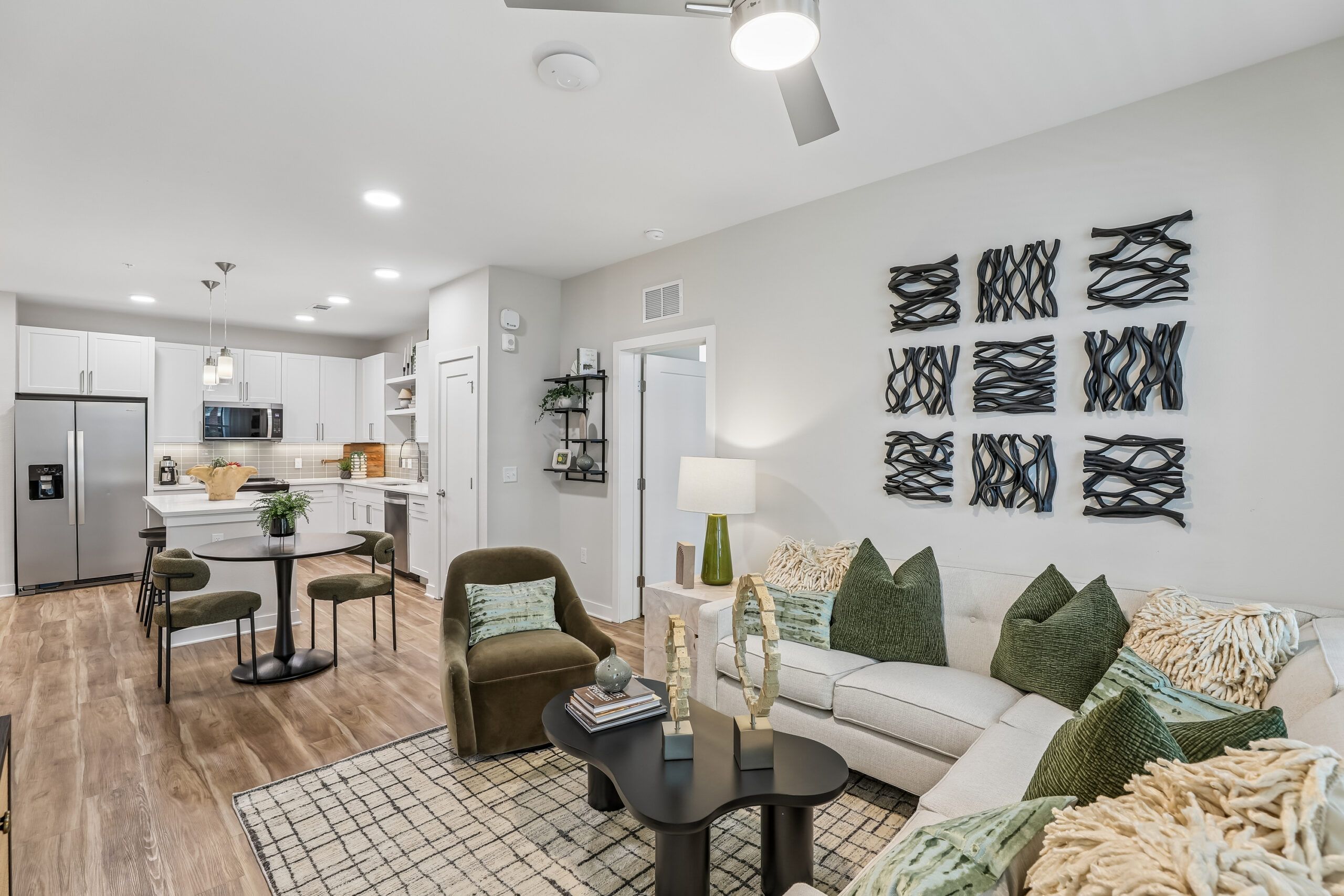 Modern open-concept living room and kitchen with green accents, wall art, and neutral furnishings.