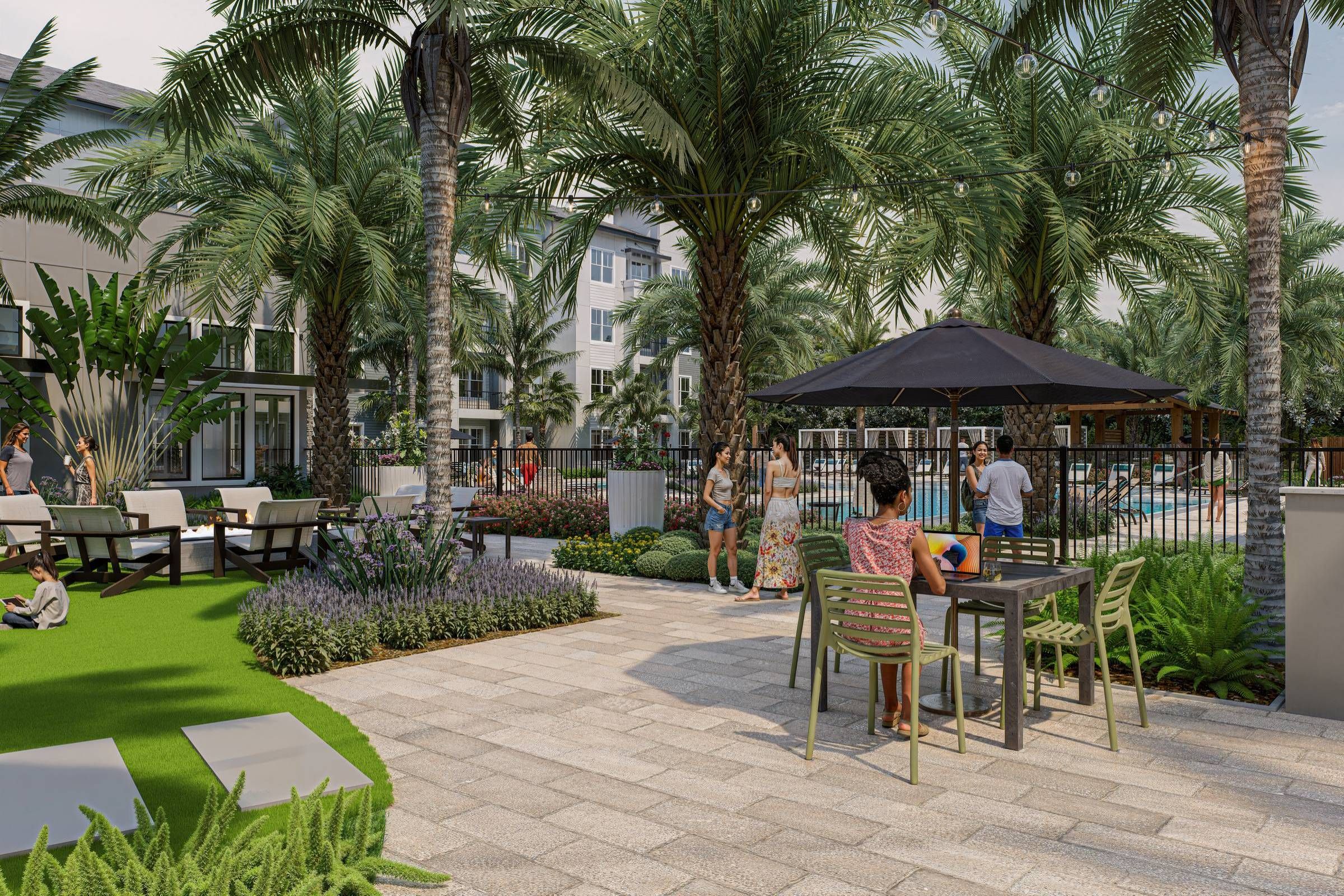 People relax and socialize in a landscaped outdoor area with palm trees, seating, and a nearby pool.